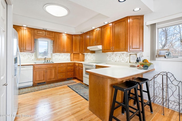 kitchen with sink, kitchen peninsula, white appliances, a breakfast bar, and light wood-type flooring