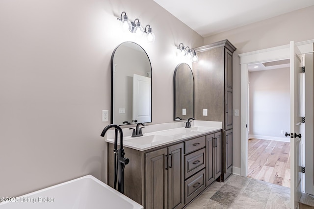 full bathroom with double vanity, a tub, baseboards, and a sink