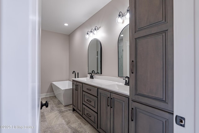 full bath with double vanity, a sink, baseboards, and a freestanding tub