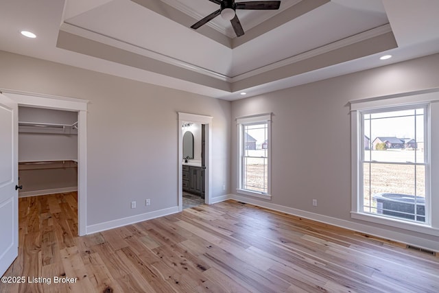 unfurnished bedroom with a spacious closet, visible vents, light wood finished floors, and a tray ceiling