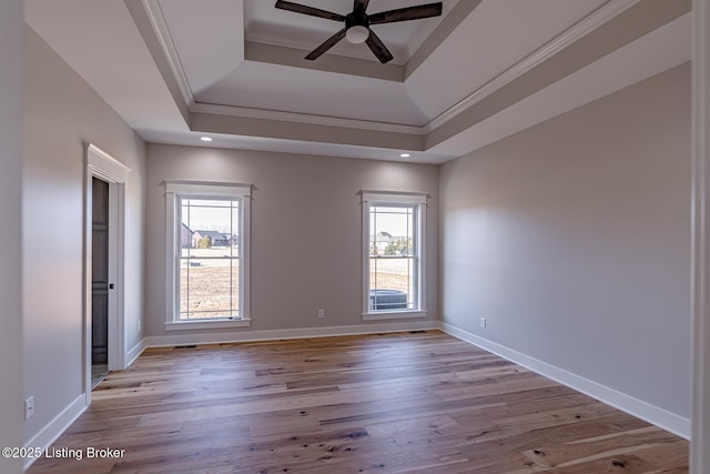 empty room featuring a raised ceiling, baseboards, light wood-type flooring, and ceiling fan