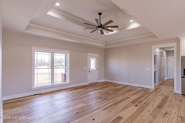 interior space featuring a tray ceiling, baseboards, ornamental molding, and light wood finished floors