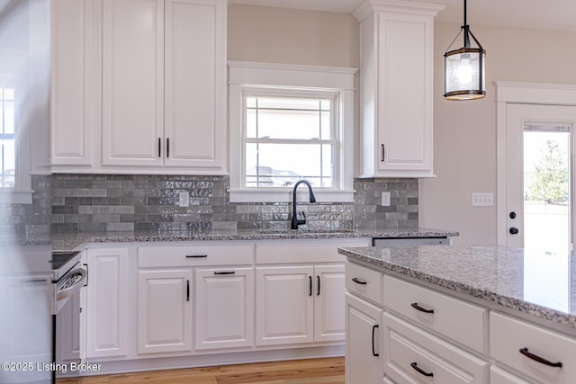 kitchen with light stone counters, a sink, stove, pendant lighting, and backsplash