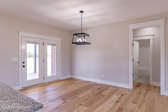 unfurnished dining area with a notable chandelier, light wood-style floors, and baseboards