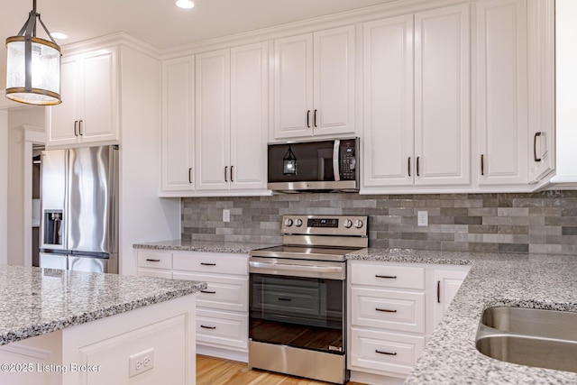 kitchen with backsplash, appliances with stainless steel finishes, hanging light fixtures, and white cabinetry