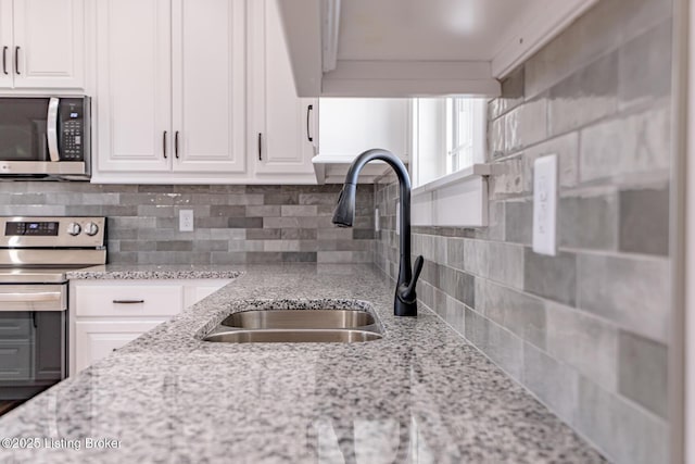 kitchen with tasteful backsplash, light stone countertops, white cabinets, stainless steel appliances, and a sink