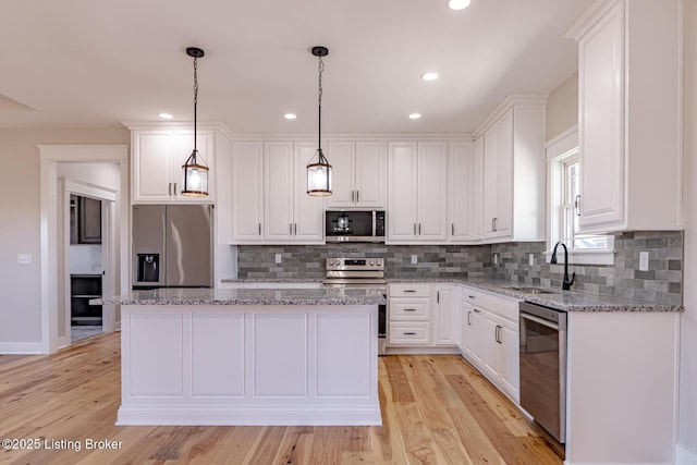 kitchen featuring a sink, light wood-style floors, appliances with stainless steel finishes, white cabinetry, and a center island