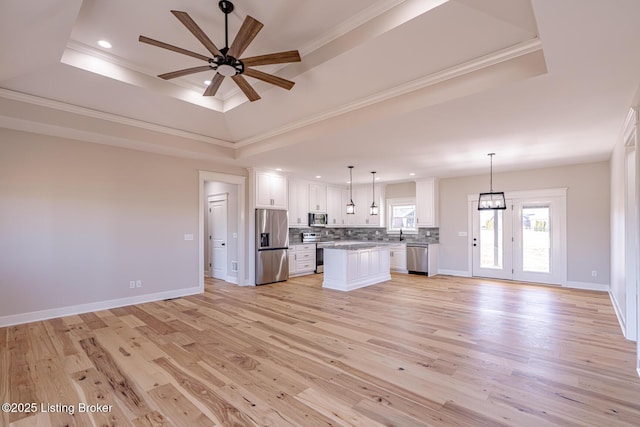 kitchen with open floor plan, appliances with stainless steel finishes, light wood finished floors, decorative backsplash, and a raised ceiling