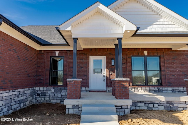 property entrance with brick siding, covered porch, and a shingled roof