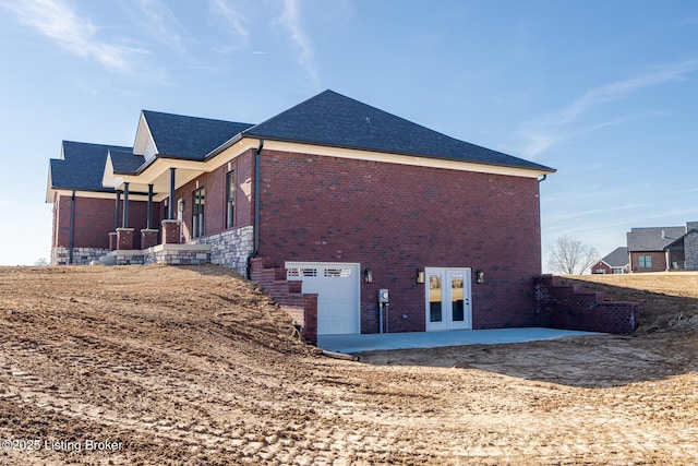 view of side of home with french doors, brick siding, a garage, and a patio area