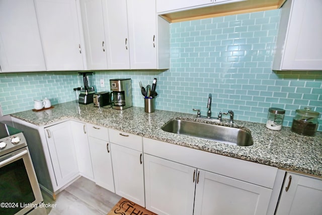 kitchen featuring stainless steel electric range, white cabinetry, sink, and tasteful backsplash