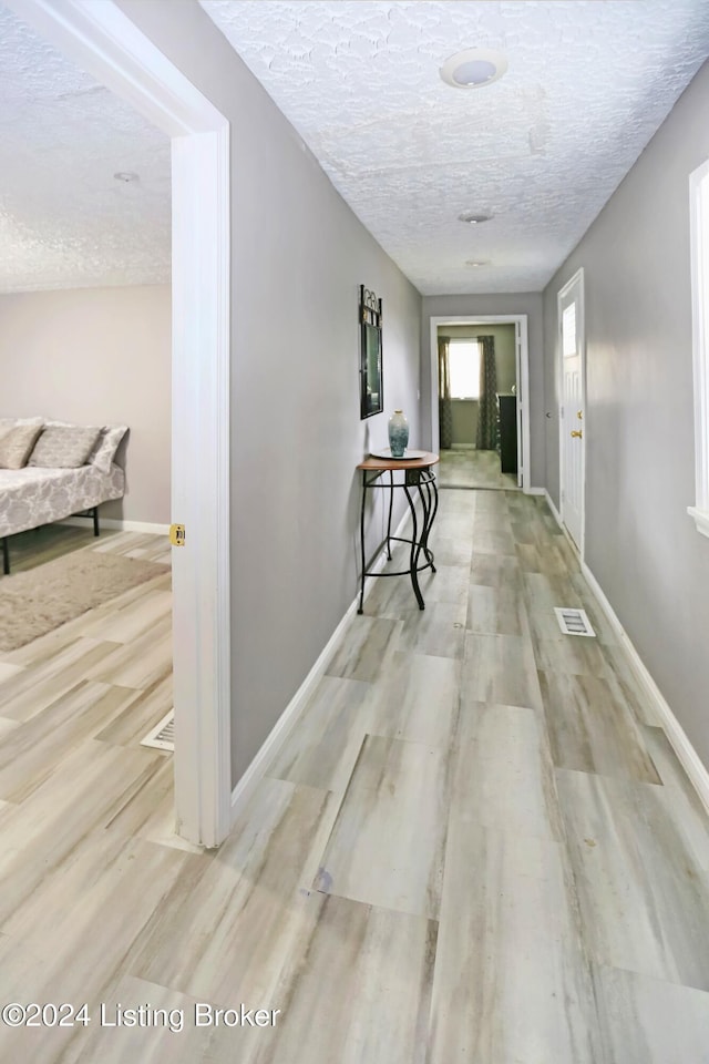 hallway with a textured ceiling and light wood-type flooring