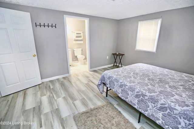 bedroom featuring ensuite bathroom, a textured ceiling, and light hardwood / wood-style flooring