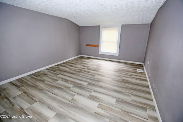 empty room with lofted ceiling, light hardwood / wood-style floors, and a textured ceiling