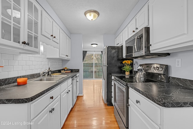 kitchen with light wood-type flooring, a textured ceiling, stainless steel appliances, sink, and white cabinetry