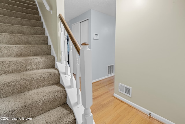 stairway with wood-type flooring and a textured ceiling