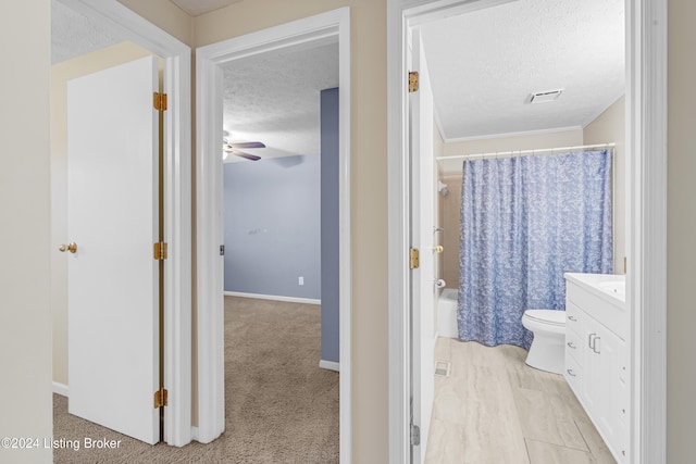 full bathroom featuring vanity, a textured ceiling, ceiling fan, shower / bathtub combination with curtain, and toilet