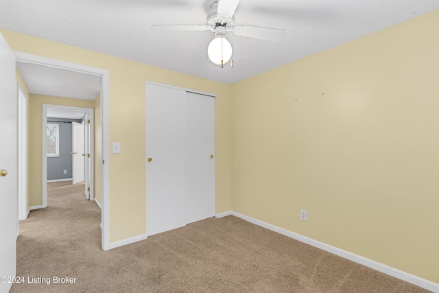 unfurnished bedroom featuring a closet, light colored carpet, and ceiling fan