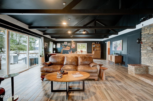 living room featuring hardwood / wood-style flooring, beam ceiling, a stone fireplace, and a wealth of natural light