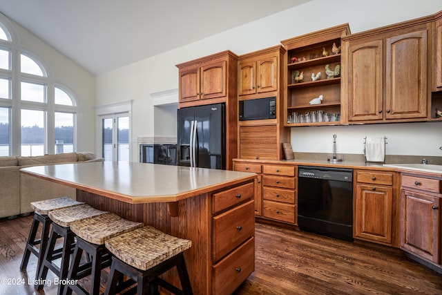 kitchen with a breakfast bar area, a center island, black appliances, and dark hardwood / wood-style floors