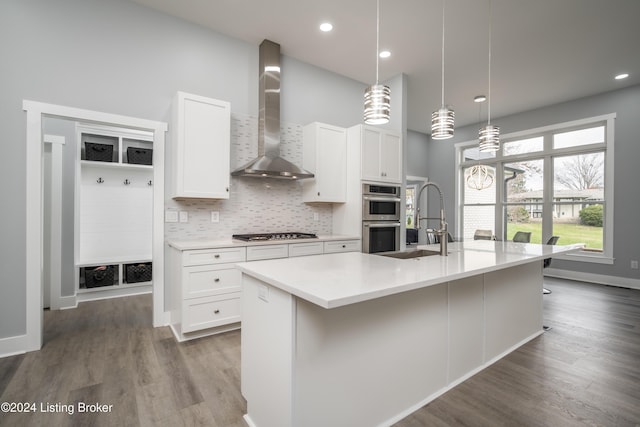 kitchen with wall chimney range hood, a kitchen island with sink, hanging light fixtures, and stainless steel appliances