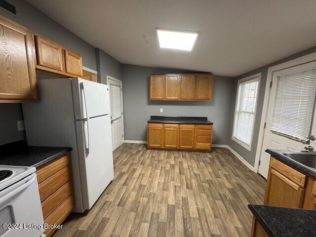 kitchen with vaulted ceiling, white appliances, sink, and light hardwood / wood-style flooring