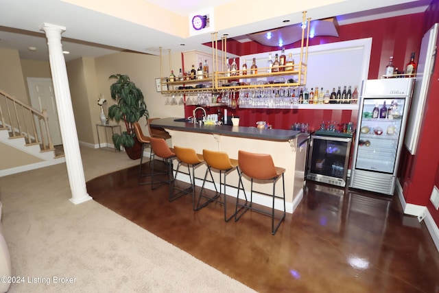 bar with decorative columns, dark carpet, beverage cooler, sink, and fridge