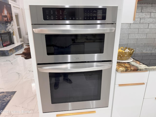 interior details with white cabinets, backsplash, and double oven