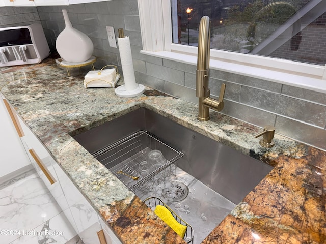 details featuring white cabinets, decorative backsplash, stone counters, and sink