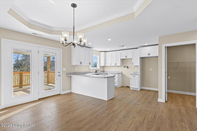 kitchen featuring pendant lighting, kitchen peninsula, hardwood / wood-style flooring, light stone counters, and white cabinetry