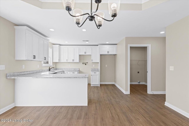 kitchen featuring kitchen peninsula, sink, a notable chandelier, hardwood / wood-style floors, and white cabinetry