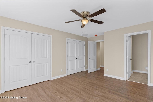 unfurnished bedroom featuring light wood-type flooring, ensuite bathroom, and multiple closets