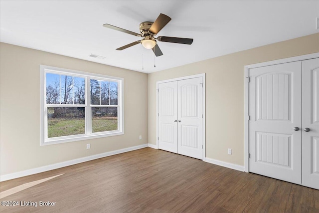 unfurnished bedroom with wood-type flooring, ceiling fan, and multiple closets