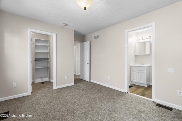 unfurnished bedroom with dark colored carpet, ensuite bathroom, a walk in closet, sink, and a textured ceiling