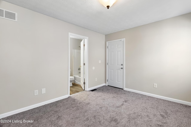 unfurnished bedroom featuring ensuite bathroom, carpet floors, and a textured ceiling