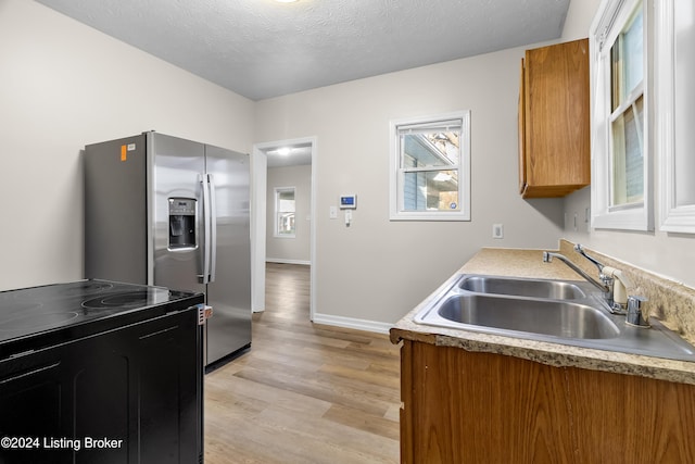 kitchen featuring sink, electric range oven, stainless steel fridge, a textured ceiling, and light wood-type flooring