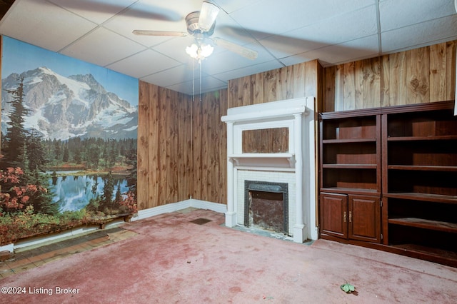 unfurnished living room featuring carpet, ceiling fan, wood walls, and a drop ceiling