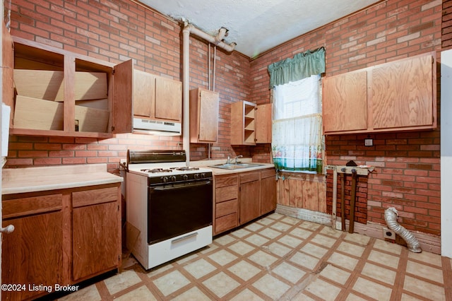 kitchen featuring brick wall, a textured ceiling, exhaust hood, and gas range gas stove