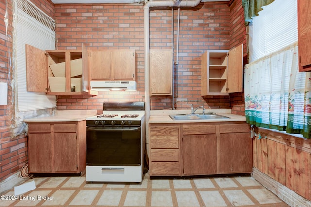 kitchen with brick wall, light tile patterned floors, white gas range oven, and sink