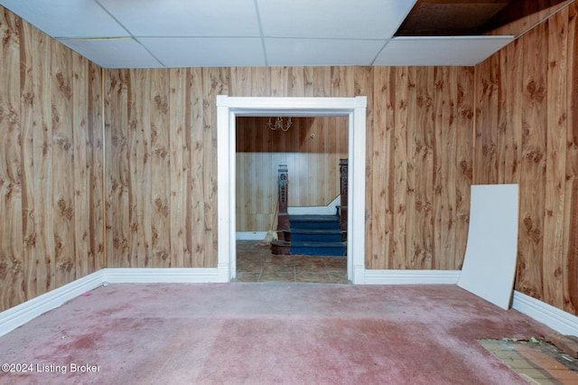 empty room featuring carpet, a drop ceiling, and wooden walls