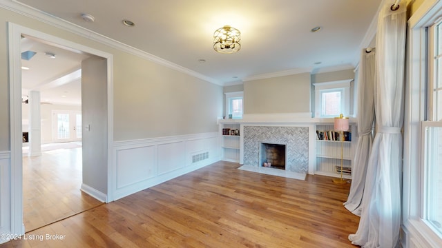 unfurnished living room featuring plenty of natural light, light hardwood / wood-style floors, crown molding, and a tiled fireplace