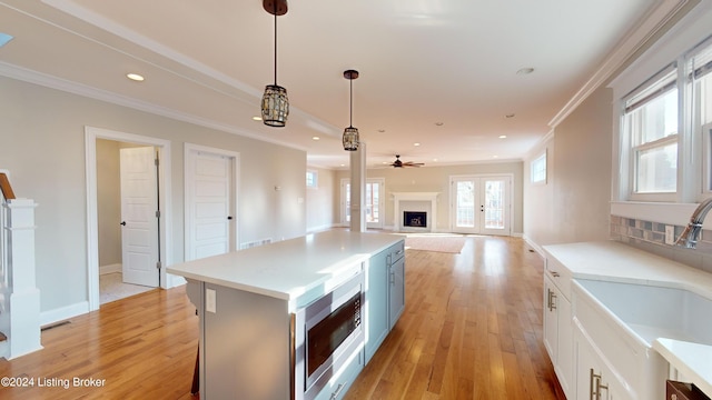 kitchen featuring stainless steel microwave, french doors, white cabinets, light wood-type flooring, and decorative light fixtures