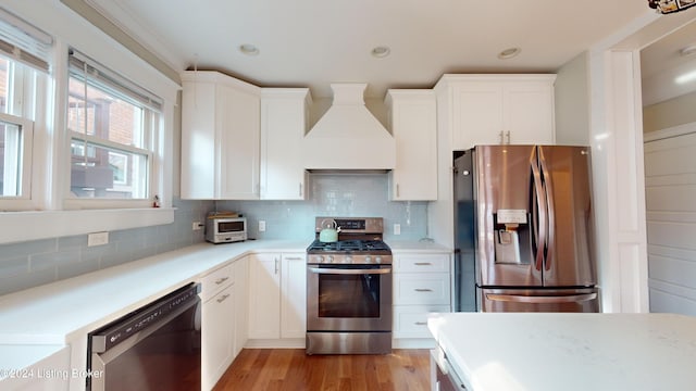 kitchen with appliances with stainless steel finishes, tasteful backsplash, custom exhaust hood, white cabinets, and light hardwood / wood-style floors