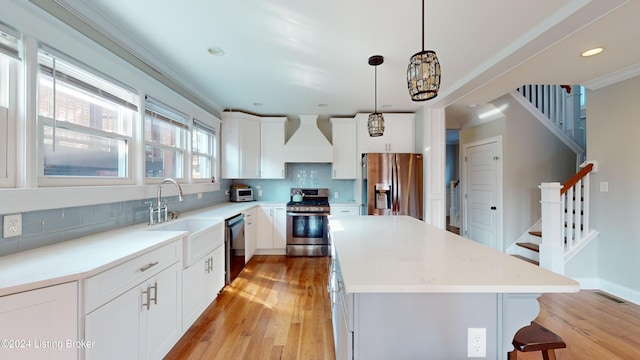 kitchen featuring stainless steel appliances, tasteful backsplash, pendant lighting, custom range hood, and light wood-type flooring