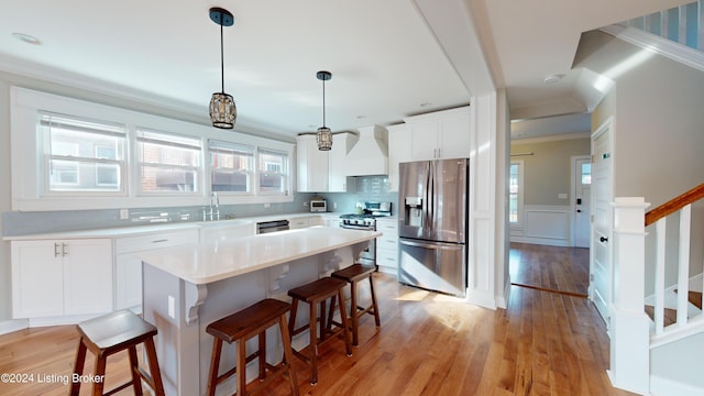 kitchen featuring a healthy amount of sunlight, stainless steel appliances, decorative light fixtures, white cabinets, and custom exhaust hood