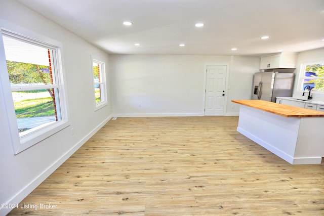 interior space with sink, stainless steel fridge with ice dispenser, butcher block countertops, light hardwood / wood-style floors, and white cabinetry