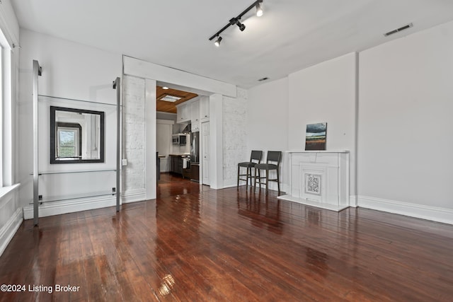 unfurnished room featuring rail lighting, a fireplace, dark wood-type flooring, and a baseboard radiator