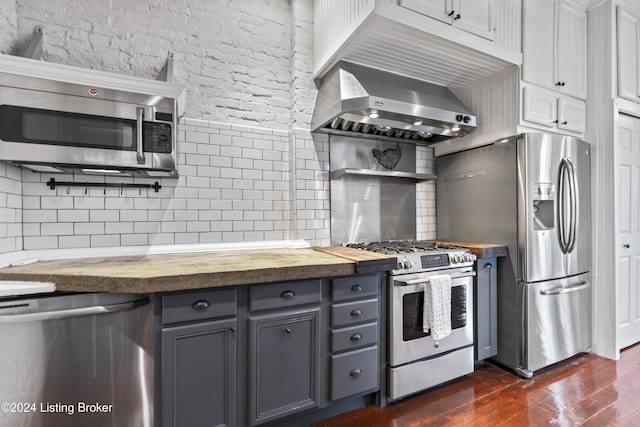 kitchen with gray cabinetry, stainless steel appliances, wall chimney range hood, tasteful backsplash, and butcher block countertops