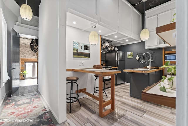 kitchen featuring light wood-type flooring, black fridge, sink, white cabinets, and hanging light fixtures