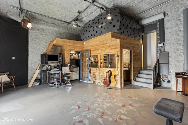 miscellaneous room featuring wood walls, a towering ceiling, and concrete floors